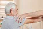 Professional male nursing assistant exercising hand of senior Caucasian man getting through physical therapy course in rehab center