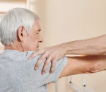 Professional male nursing assistant exercising hand of senior Caucasian man getting through physical therapy course in rehab center